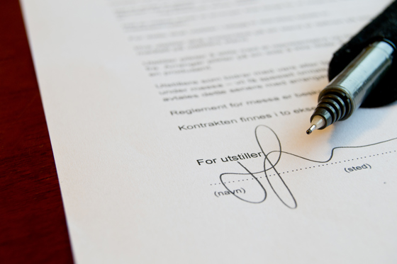 Et stykke papir med en underskrift og en kuglepen liggende ved siden af.