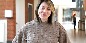 Justina står front mod kameraet med et lille smil. Hun er iført en lys, brun bluse og har mellemlangt hår. 