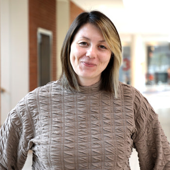 Justina står front mod kameraet med et lille smil. Hun er iført en lys, brun bluse og har mellemlangt hår. 