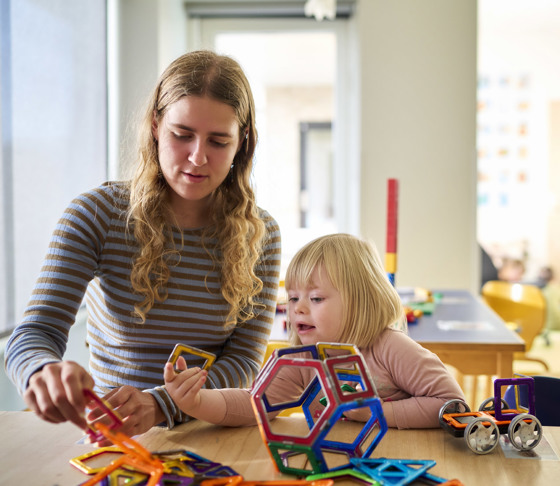 En pædagogisk assistent leger med magnetiske figurer sammen med en lille pige.