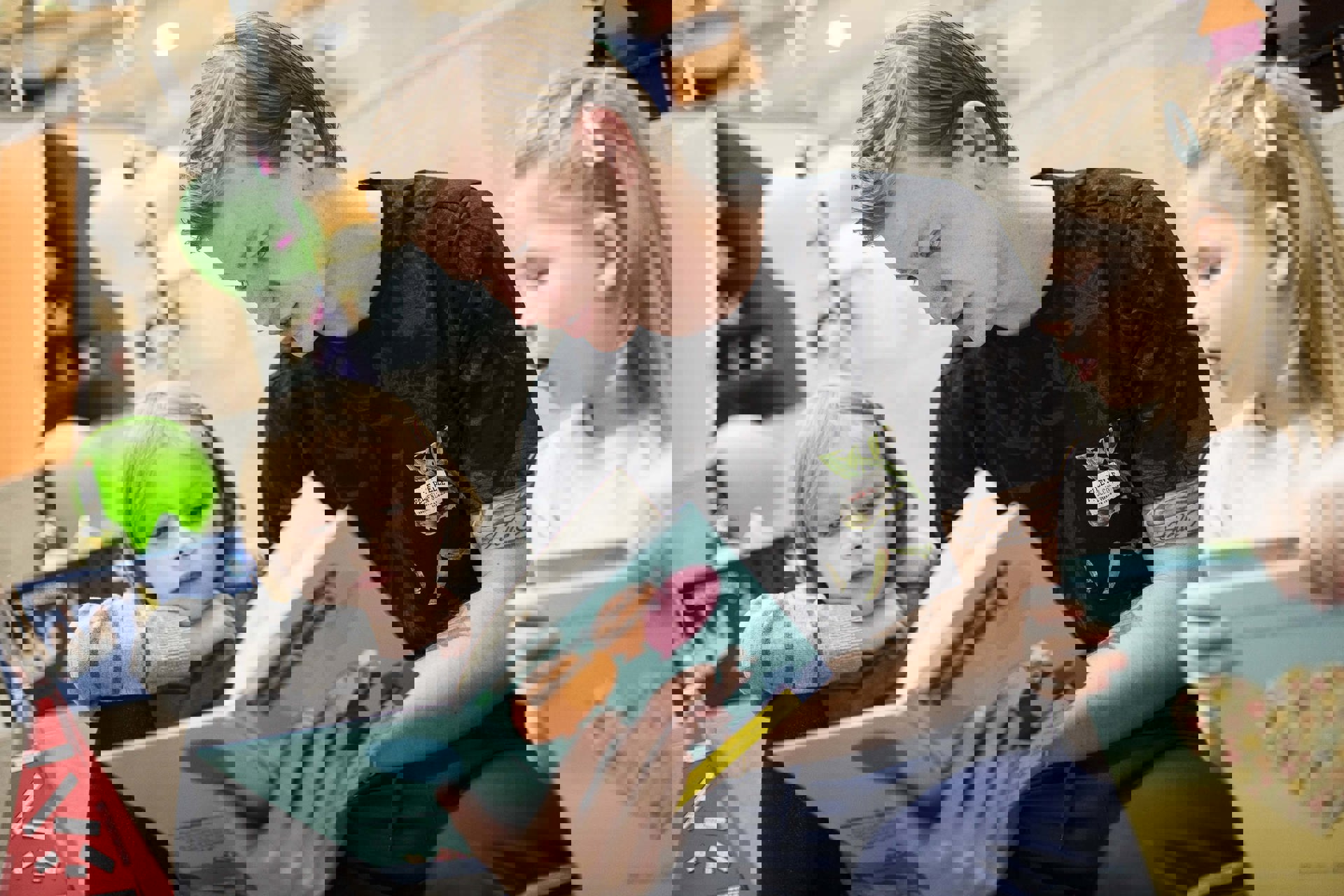 En ung mand sidder med en opslået bog i hænderne og læser op for to børn, der sidder på hver side af ham. Børnene følger interesseret med og har fokus rettet mod bogen. 