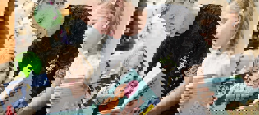 En ung mand sidder med en opslået bog i hænderne og læser op for to børn, der sidder på hver side af ham. Børnene følger interesseret med og har fokus rettet mod bogen. 